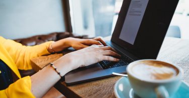 woman in yellow jacket typing on laptop