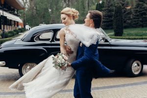 luxury wedding couple dancing at old car in light. stylish bride and groom hugging and embracing in city street. romantic passionate sensual moment. woman and man together