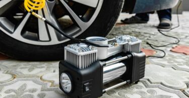 A black and gray portable tire inflator on a carpeted floor hooked up to a car tire via a yellow air hose.