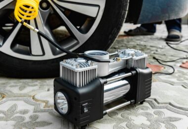 A black and gray portable tire inflator on a carpeted floor hooked up to a car tire via a yellow air hose.