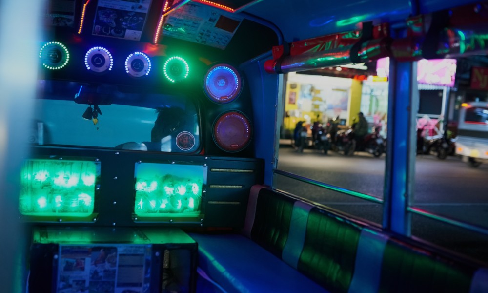 The interior of a party bus illuminated by bright blue, green, and red LED strips, with comfortable seating lining the walls.