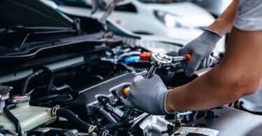 A car mechanic using a torque wrench to tighten a bolt on the engine of a vehicle. He is wearing gray gloves.