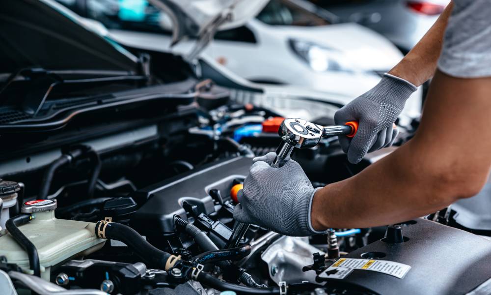 A car mechanic using a torque wrench to tighten a bolt on the engine of a vehicle. He is wearing gray gloves.