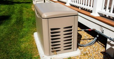 A tan, rectangular whole-home generator on a concrete pad next to a backyard deck connected to a fuel pipeline.