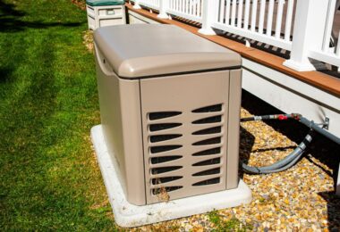 A tan, rectangular whole-home generator on a concrete pad next to a backyard deck connected to a fuel pipeline.