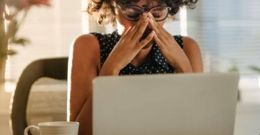 A woman feeling stressed while working on her laptop at home, symbolising the challenges of managing stress and turning it into a springboard for success.