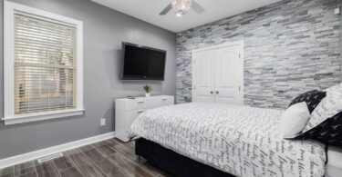 Modern teenager's bedroom featuring a stylish bed with patterned bedding, a stone accent wall, and a wooden floor, ideal for illustrating how aluminium shutters can transform a teen's personal space.