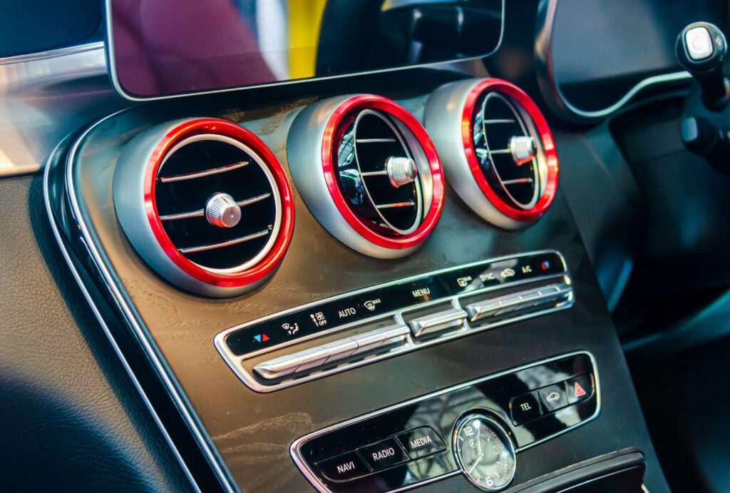 Close-up view of a car's air conditioning control panel with illuminated red dials and metallic accents, symbolising the readiness of a truck's AC system for a long road trip after being idle.