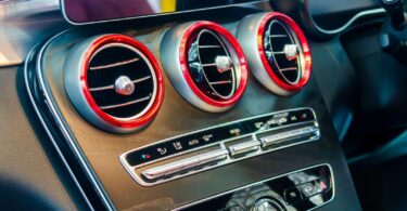 Close-up view of a car's air conditioning control panel with illuminated red dials and metallic accents, symbolising the readiness of a truck's AC system for a long road trip after being idle.