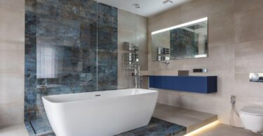 A sleek and modern bathroom featuring a standalone tub, innovative glass shower, and blue vanity, highlighting modern conveniences and design aesthetics.