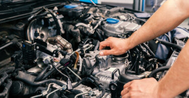 A mechanic works on upgrading an engine. The hood is open and they use a wrench on one of the engine components.