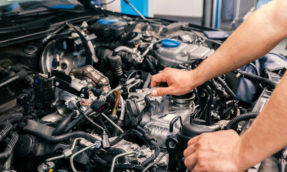 A mechanic works on upgrading an engine. The hood is open and they use a wrench on one of the engine components.