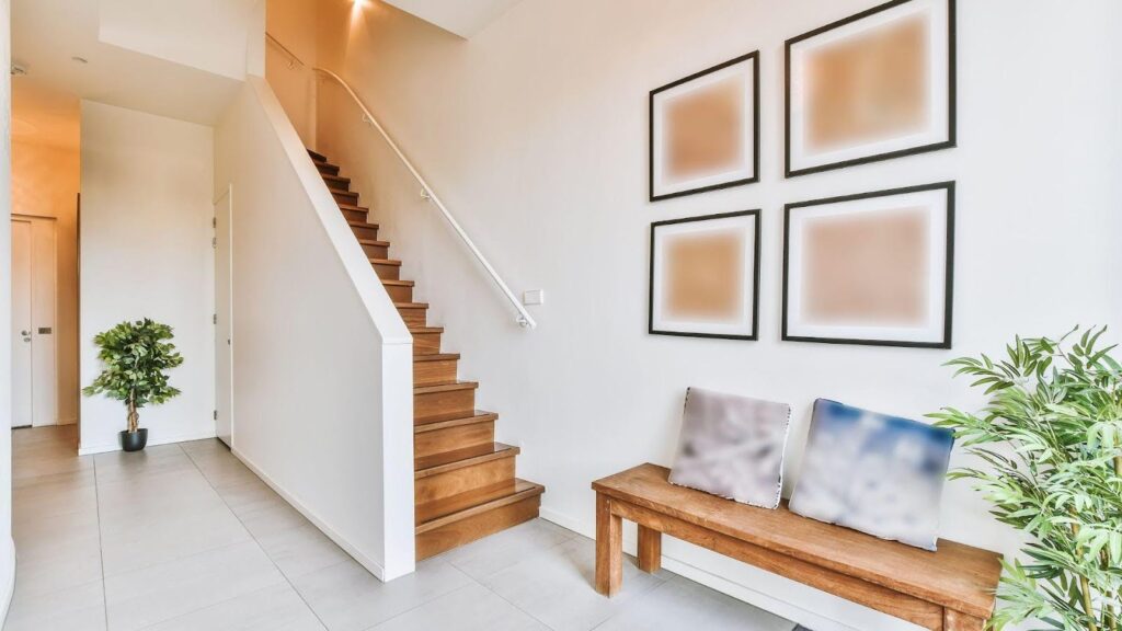 A modern home interior showcasing one of 2024's emerging staircase designs featuring wooden steps, a white railing, and a minimalist decor style with abstract wall art and potted plants enhancing the area. 