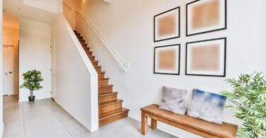 A modern home interior showcasing one of 2024's emerging staircase designs featuring wooden steps, a white railing, and a minimalist decor style with abstract wall art and potted plants enhancing the area.