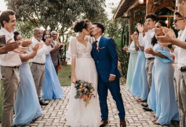 A bride and groom kissing, surrounded by cheering guests at an outdoor wedding celebration, capturing a moment of joy and community support.