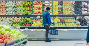 A young and stylish man shops the produce aisle at his local grocery store. The produce is fresh and displayed well.