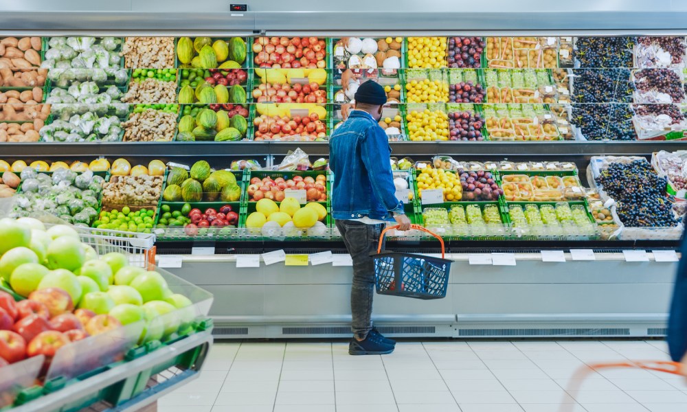 A young and stylish man shops the produce aisle at his local grocery store. The produce is fresh and displayed well.