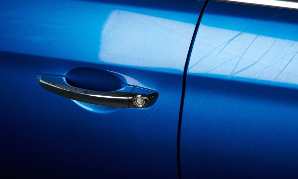 A blue car with a black handle and silver keyhole on the door. There are scuffs and scratches all along the side.