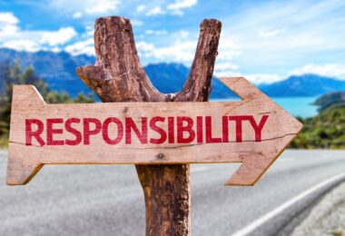 A dead wooden tree next to the road holds up a sign in the shape of an arrow that reads "RESPONSIBILITY" in red letters.