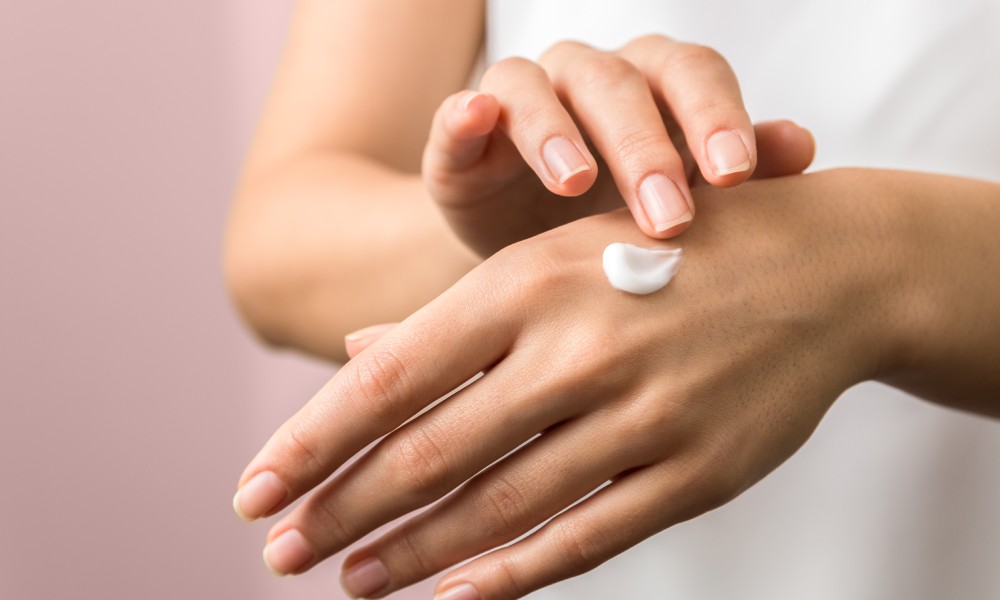 A beauty guru applying a hand cream onto their hands. The backdrop is pink and they are showing both hands.