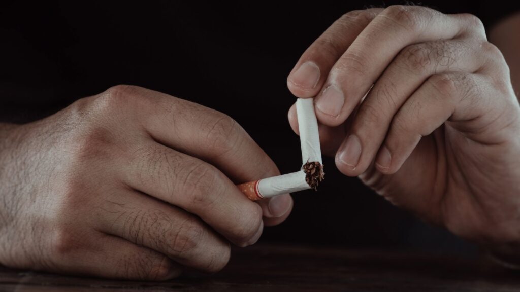 A close-up of a man's hands breaking a cigarette in half, representing wellness alternatives for the overworked instead of smoke breaks.