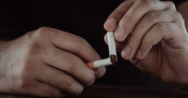 A close-up of a man's hands breaking a cigarette in half, representing wellness alternatives for the overworked instead of smoke breaks.