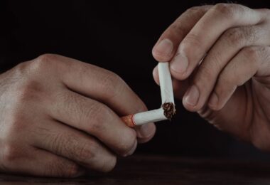 A close-up of a man's hands breaking a cigarette in half, representing wellness alternatives for the overworked instead of smoke breaks.