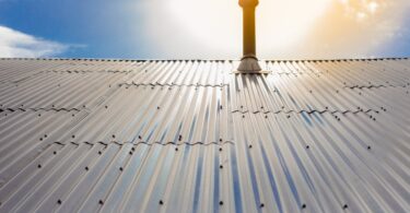 Aluminum panels drilled onto the roof of a building. There is a roof pole sticking out from the metal panels on the roof.