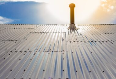 Aluminum panels drilled onto the roof of a building. There is a roof pole sticking out from the metal panels on the roof.