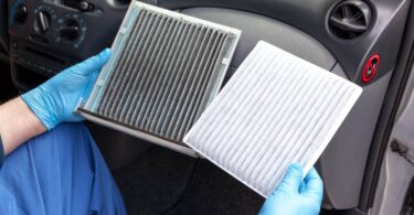 A person sitting in a car and holding two cabin air filters. One air filter is dirty and the other one is clean.