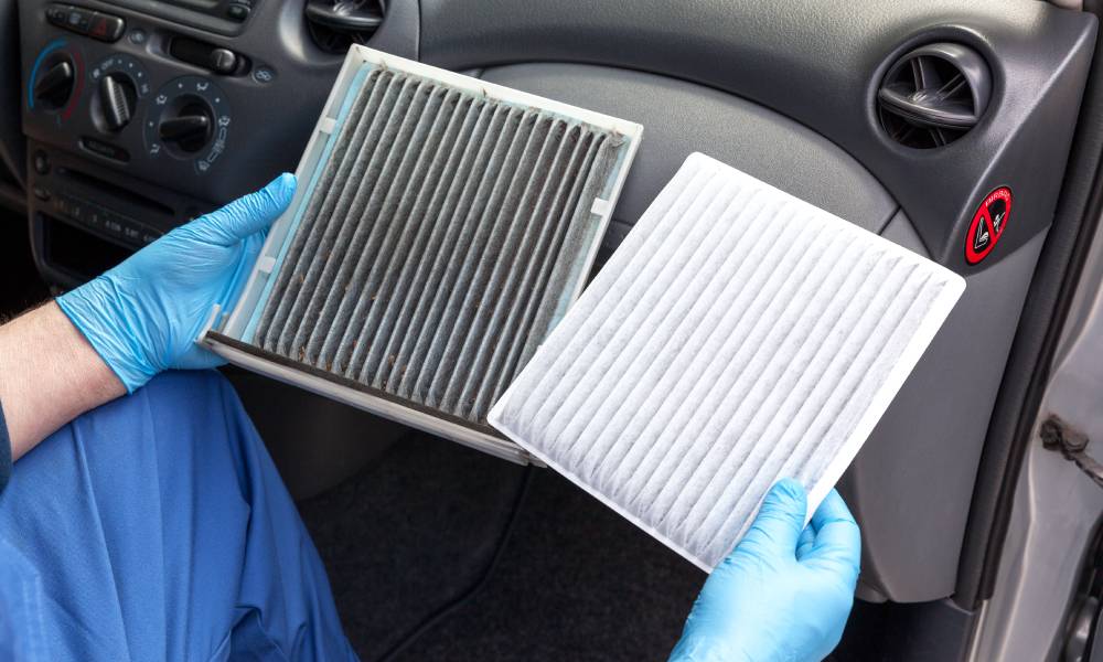 A person sitting in a car and holding two cabin air filters. One air filter is dirty and the other one is clean.