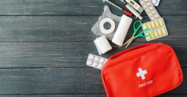 Essential first aid supplies including bandages, scissors, tape, and medications displayed alongside a red first aid kit on a wooden background