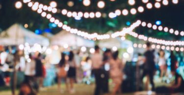 A blurred gathering of various people celebrating a non-descript holiday while outdoors at a tented festival.