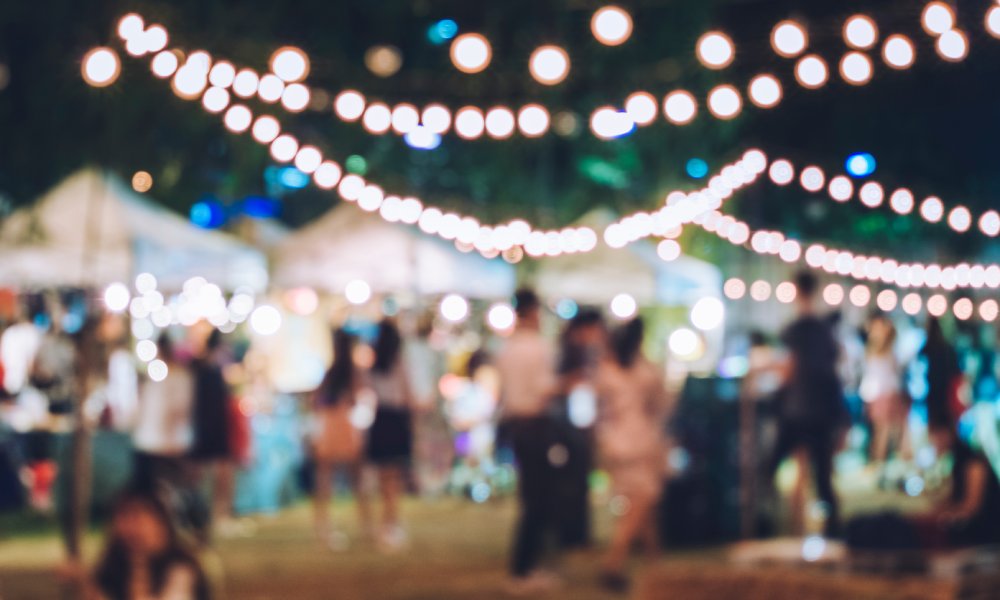 A blurred gathering of various people celebrating a non-descript holiday while outdoors at a tented festival.