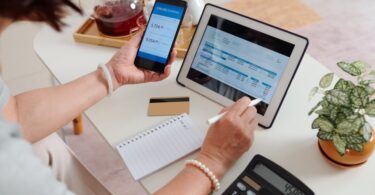 A close-up of the hands of a woman checking their utility bill on a tablet computer and calculating their bills.