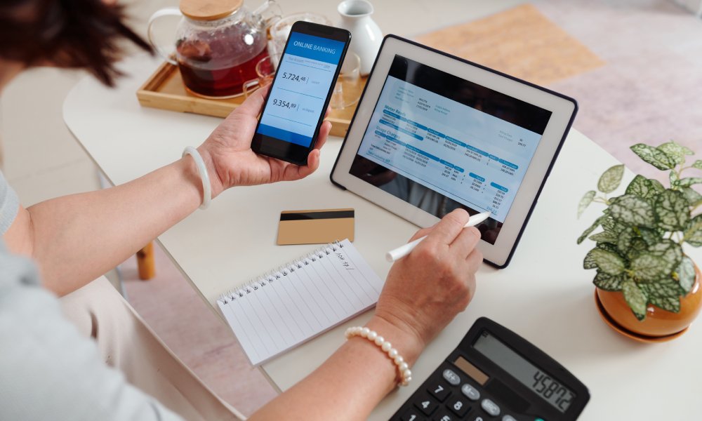 A close-up of the hands of a woman checking their utility bill on a tablet computer and calculating their bills.