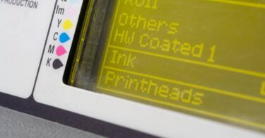 A digital screen with the words "Roll," "Others," "HW Coated 1," "Ink," and "Printheads." There is a color guide on the side.