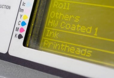 A digital screen with the words "Roll," "Others," "HW Coated 1," "Ink," and "Printheads." There is a color guide on the side.