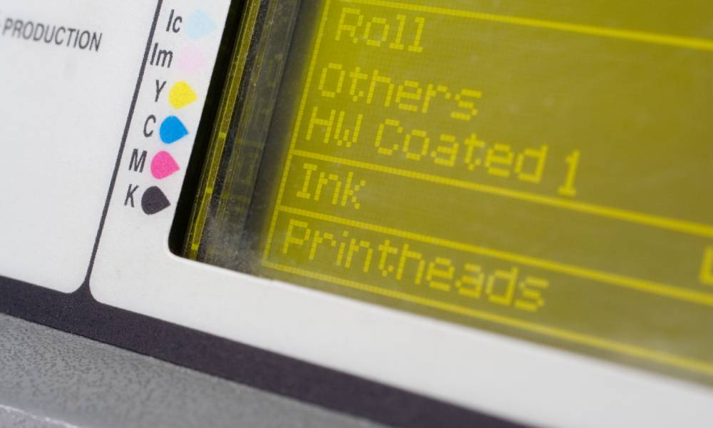 A digital screen with the words "Roll," "Others," "HW Coated 1," "Ink," and "Printheads." There is a color guide on the side.