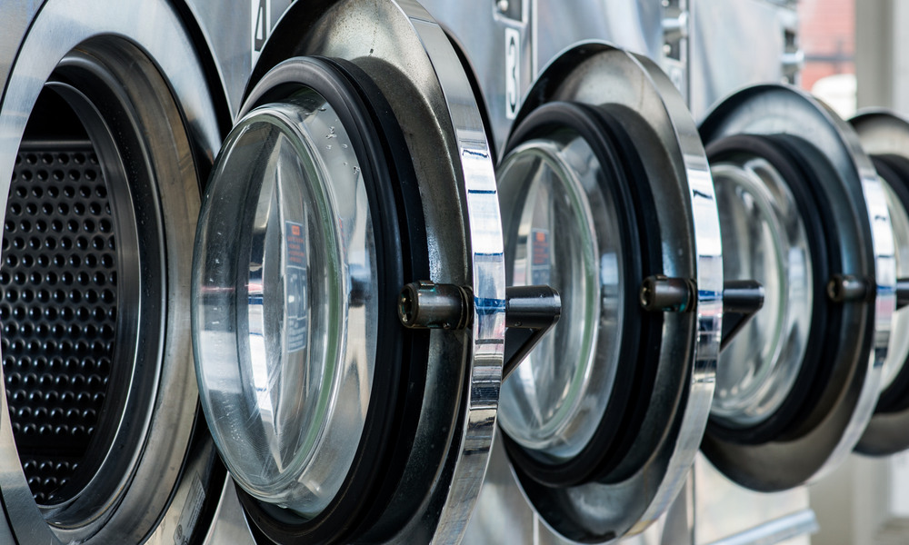 Four steel front-loaded laundry machines in a laundry facility with their round doors swung open.